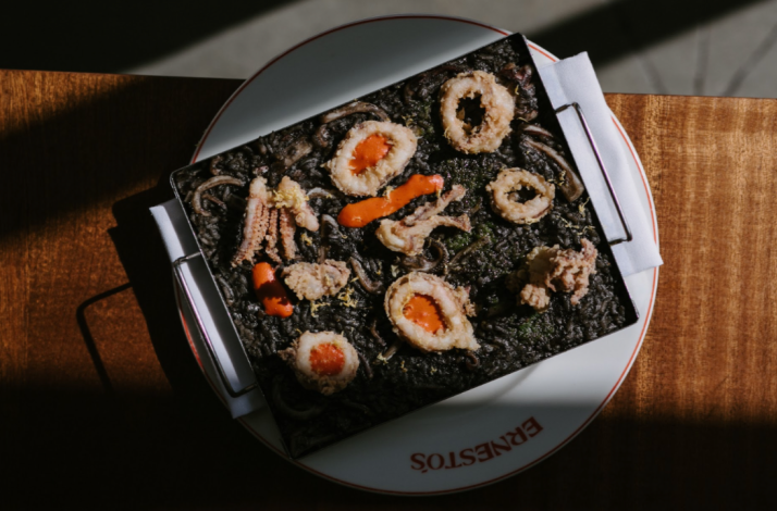 Dark squid ink seafood rice dish with calamari and bright orange sauce, served in a pan at Ernesto's.