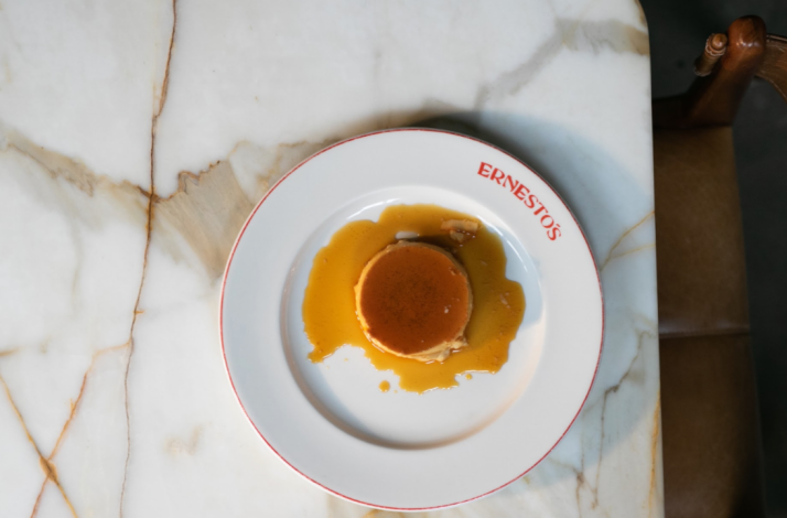 Classic caramel flan topped with amber sauce on an Ernesto's branded white plate, viewed from above.