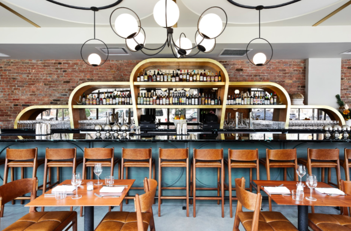 Warm-toned interior at Ernesto's with a curved gold bar, globe pendant lighting, and set dining tables.