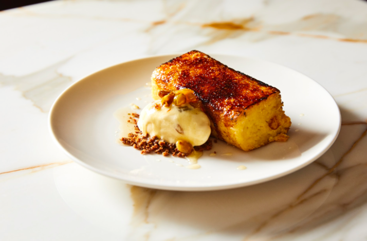 Caramelized golden-crusted dessert slice served with cream and crushed nuts on a white plate at Ernesto's.