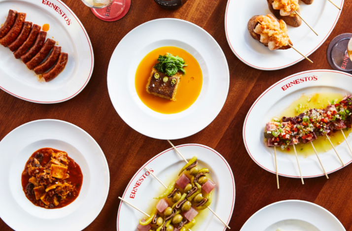 Variety of Ernesto's signature Basque-inspired dishes arranged on a wooden table, including skewers and stewed plates.