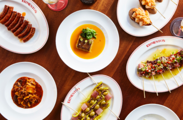 Variety of Ernesto's signature Basque-inspired dishes arranged on a wooden table, including skewers and stewed plates.