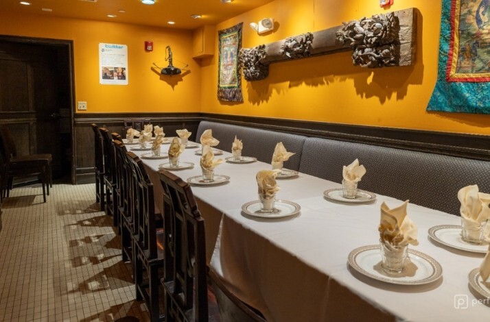A long dining table set with white tablecloths alongside a banquette against yellow walls at Fang Restaurant.