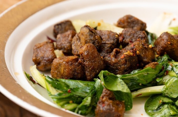 Stir-fried beef short ribs served over bok choy greens on a white rimmed plate at Fang Restaurant.