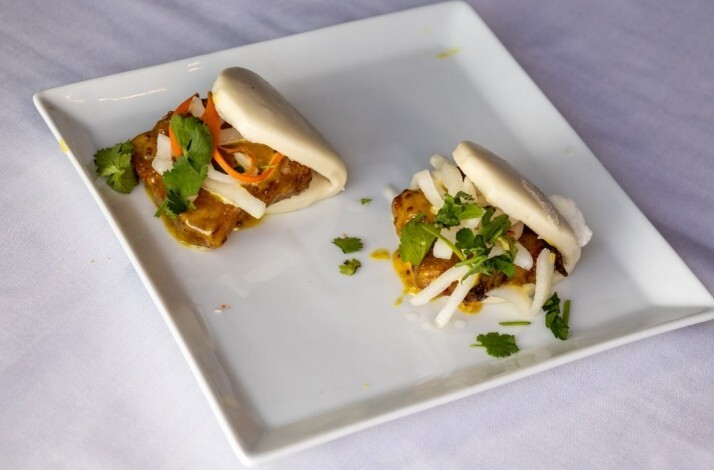 Two pork belly bao buns topped with cilantro and pickled vegetables on a white plate at Fang Restaurant.