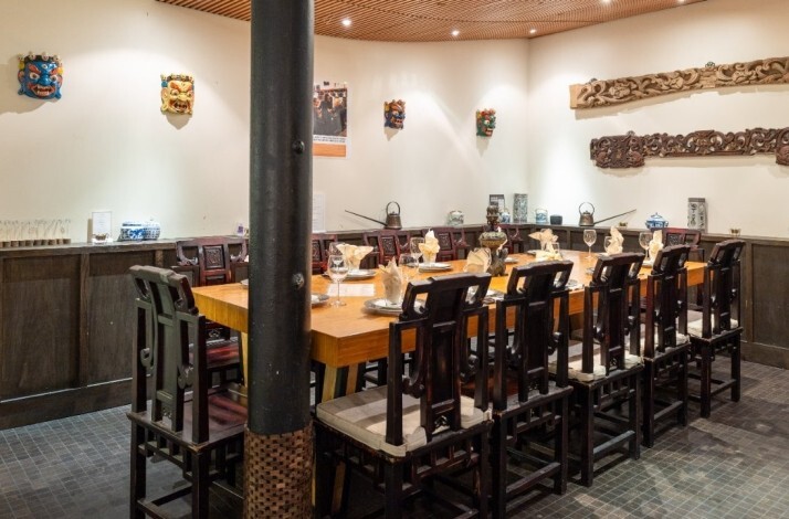 A long wooden table set for group dining in a private room decorated with colorful masks at Fang Restaurant.