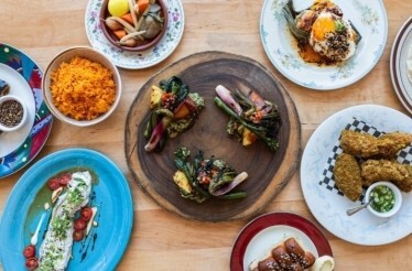 Overhead spread of plated dishes including orange rice, fried chicken, greens, and sauced entrées served at Prubechu.