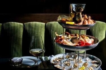 JouJou's seafood tower featuring fresh oysters, whole crab, prawns, and caviar vessel across three tiers, paired with chilled white wine.