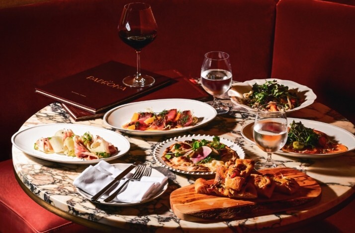 La Padrona Boston marble table set in a red velvet booth, displaying Italian antipasti, flatbreads, salads, and wine.
