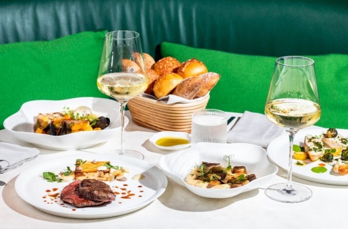 Dinner spread at Le Jardinier featuring steak, fish, vegetable dishes, white wine, and artisan bread on a set table. 