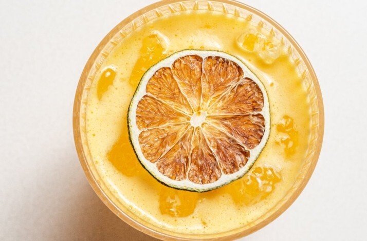 Overhead view of a golden frothy cocktail in a coupe glass garnished with a charred lime half at Le Jardinier.
