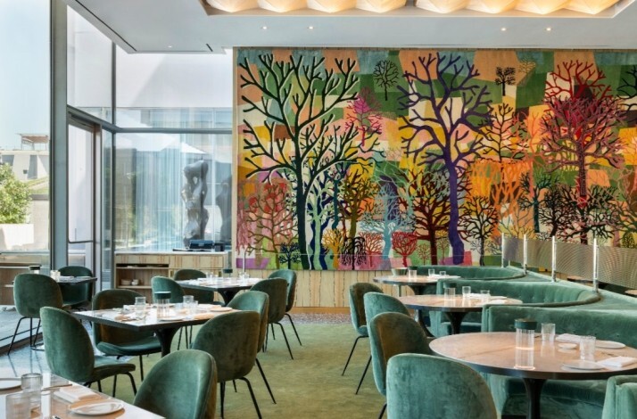Sunlit dining room with green velvet seating and a colorful tree mural at Le Jardinier Houston.