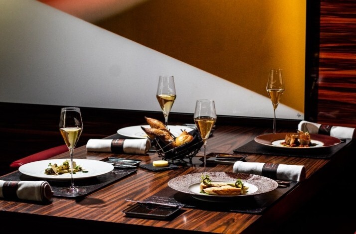 Elegant dining table set with champagne flutes and plated courses in a warm, modern dining room at L’Atelier Miami.