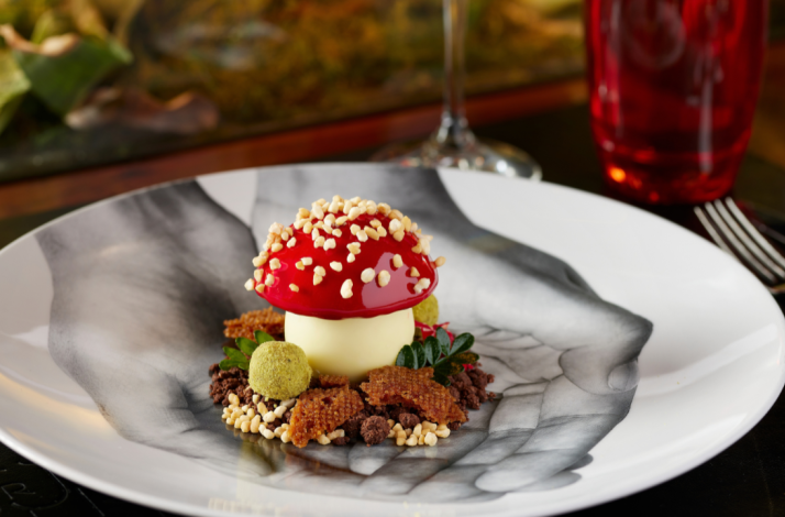 Artfully plated mushroom-shaped dessert with glossy red cap and crisp garnishes on a black-and-white patterned plate.