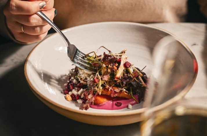 A plated salad with roasted vegetables, microgreens, and a vibrant pink puree, served in a wide ceramic bowl.