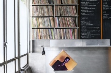 Record shelf behind a metal counter; chalkboard menu at right and a vinyl sleeve leaning in front.