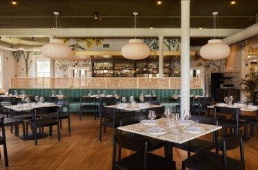 Bright restaurant dining room with marble-topped tables, green velvet banquettes at Dalida restaurant. 