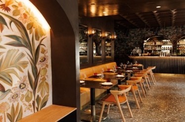 Moody dining room with floral wall mural, candlelit tables, and a curved back bar lined with bottles at Maria Isabel.