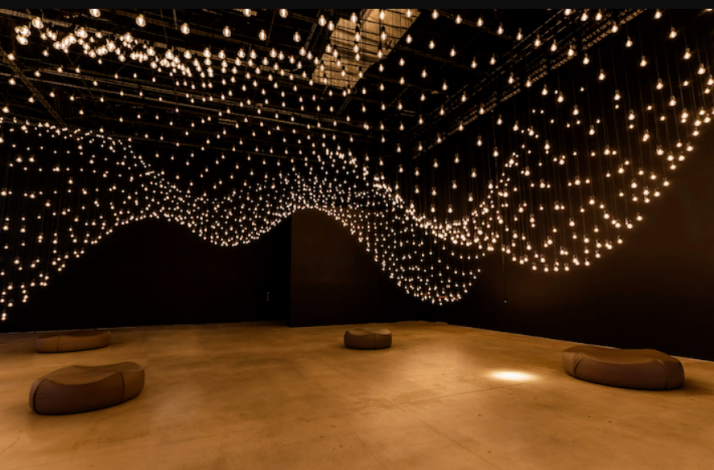 Immersive gallery space featuring a wave-like canopy of suspended glowing bulbs.