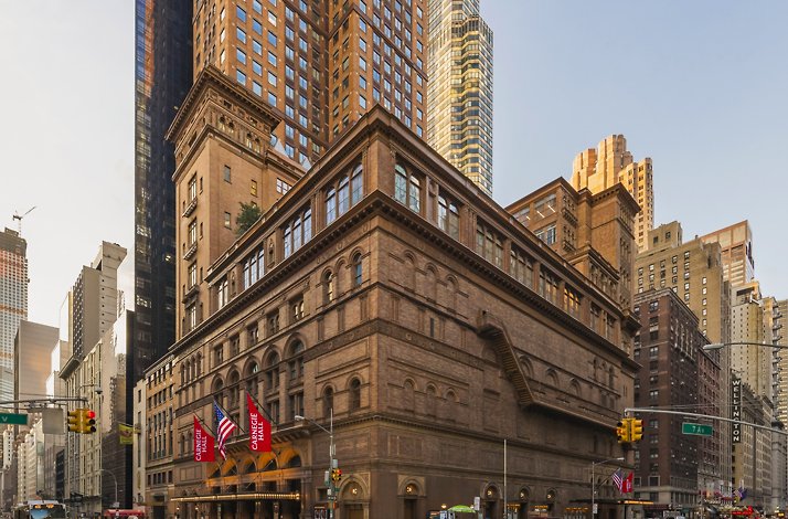 Carnegie Hall landmark facade glowing at dusk, red venue banners flanking the entrance amid the Manhattan skyline. © Jeff Goldberg / Esto.