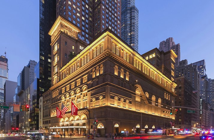 Illuminated exterior of Carnegie Hall at night with street traffic. 