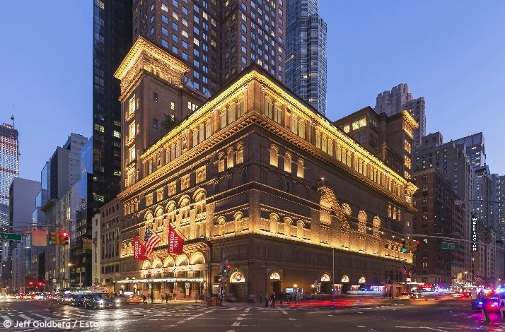 Carnegie Hall landmark facade glowing at dusk, red venue banners flanking the entrance amid the Manhattan skyline. © Jeff Goldberg / Esto.