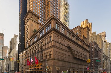 Carnegie Hall landmark facade glowing at dusk, red venue banners flanking the entrance amid the Manhattan skyline. © Jeff Goldberg / Esto.