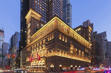 Illuminated exterior of Carnegie Hall at night with street traffic. 