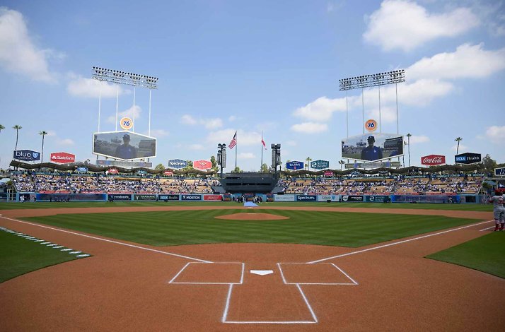 Dodger Stadium infield viewed from home plate, with filled stands and twin scoreboards under a sunny sky.