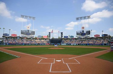 Dodger Stadium infield viewed from home plate, with filled stands and twin scoreboards under a sunny sky.