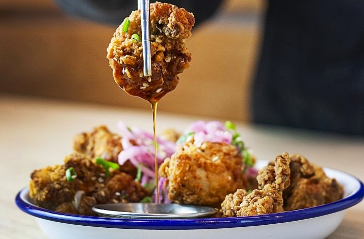 Close shot of Korean Fried chicken, Chikin being served, a piece is being lifted with chopsticks showing a sauce dripping from the chicken piece