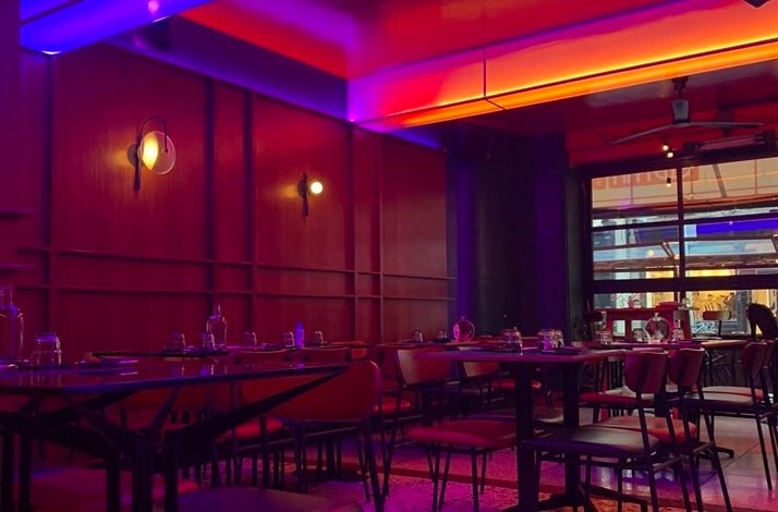 Restaurant interior with dark wood-paneled walls, vibrant purple-pink lighting, and cozy tables.