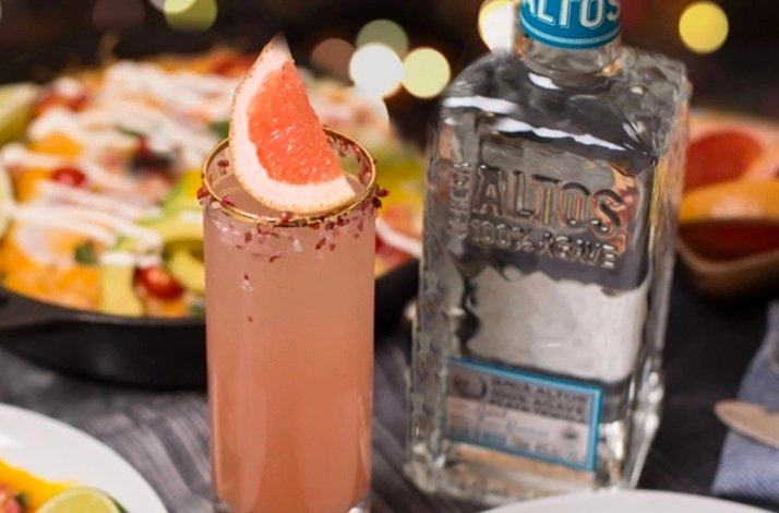 Paloma cocktail garnished with grapefruit wedge beside an Altos 100% Agave tequila bottle.