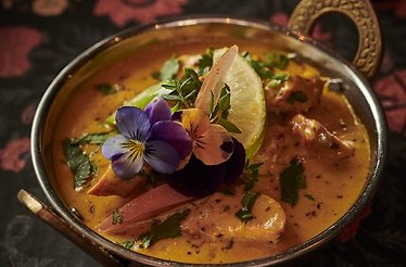 Rich curry served in a traditional balti bowl, garnished with edible pansy flowers and a lime wedge at DAATA, Sandymount.