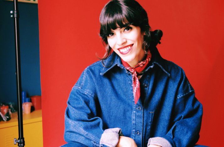 Coco Dávez poses for a photo against a red background.