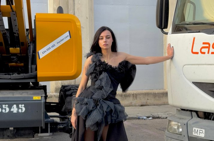 Woman in a black dress posing by construction vehicles.
