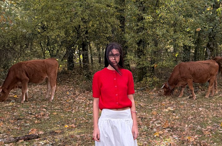 Woman in a red top standing in a forest with cows.