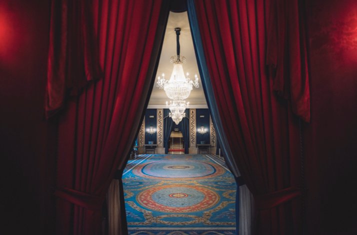 Ornate hall with red curtains, blue carpet, and grand chandeliers at Teatro Real.