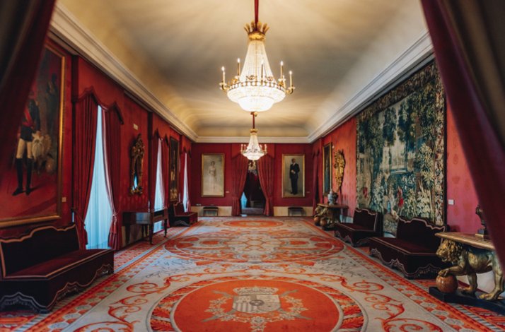 Luxurious red lounge with chandeliers, portraits, and detailed carpet at Teatro Real.
