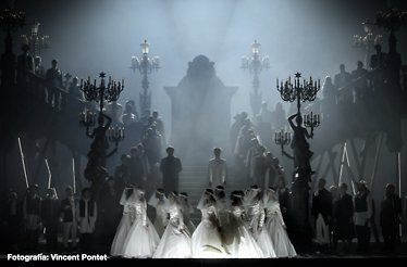 Brides in white gowns dance before a grand staircase shrouded in mist and cold light in Romeo and Juliette. Photo by Vincent Pontet