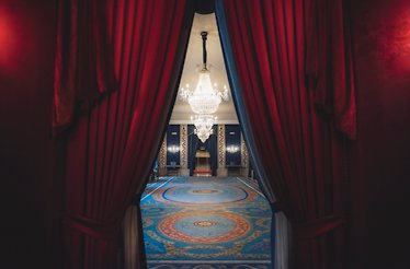 Ornate hall with red curtains, blue carpet, and grand chandeliers at Teatro Real.