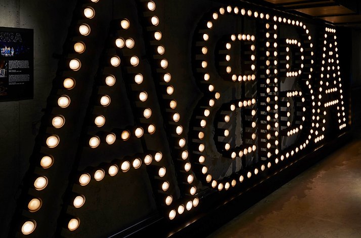 Large illuminated ABBA sign lights up a dark museum hallway.