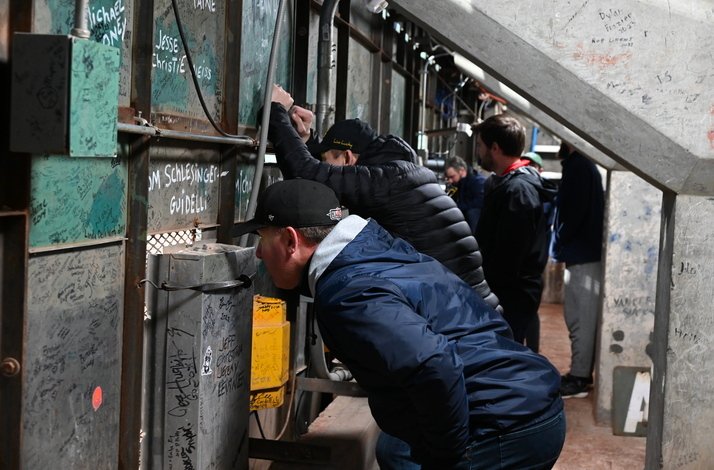 A man leans over a wall, peering intently at something on the other side.