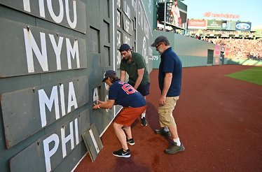  Three men are writing on a sign while attending a baseball game, focused on their task amidst the crowd.