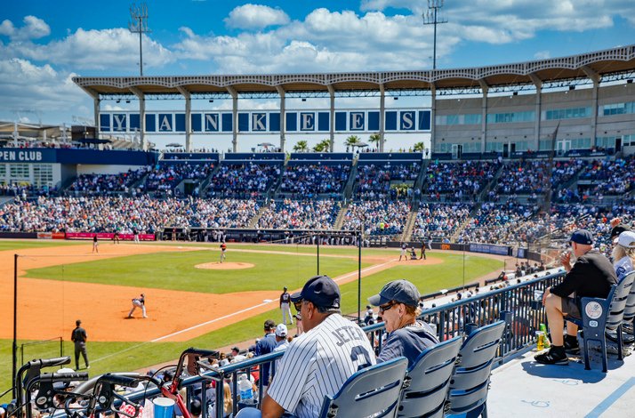 Fans fill the stands at Yankee Stadium during a sunny day baseball game.