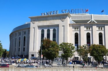 Exterior of Yankee Stadium on a sunny game day, with crowds of fans gathered outside the iconic facade.