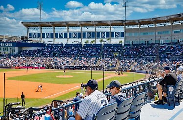 Fans fill the stands at Yankee Stadium during a sunny day baseball game.