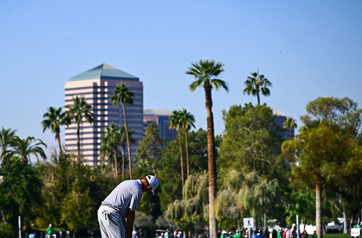  golfer putting on a green against a backdrop of palm trees and a tall building.