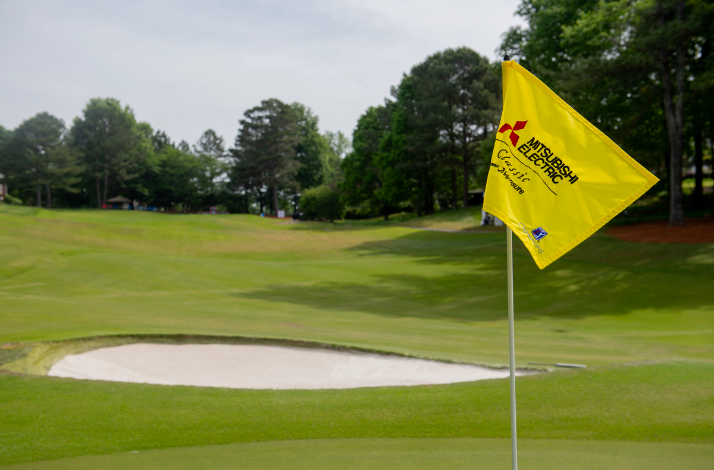 A golf course with a yellow flag featuring the Mitsubishi Electric Classic logo.