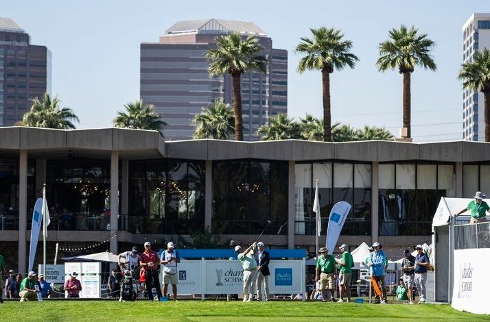 Golfer teeing off at a PGA Tour Champions event, with Charles Schwab banners, spectators, palm trees, and a city skyline behind.